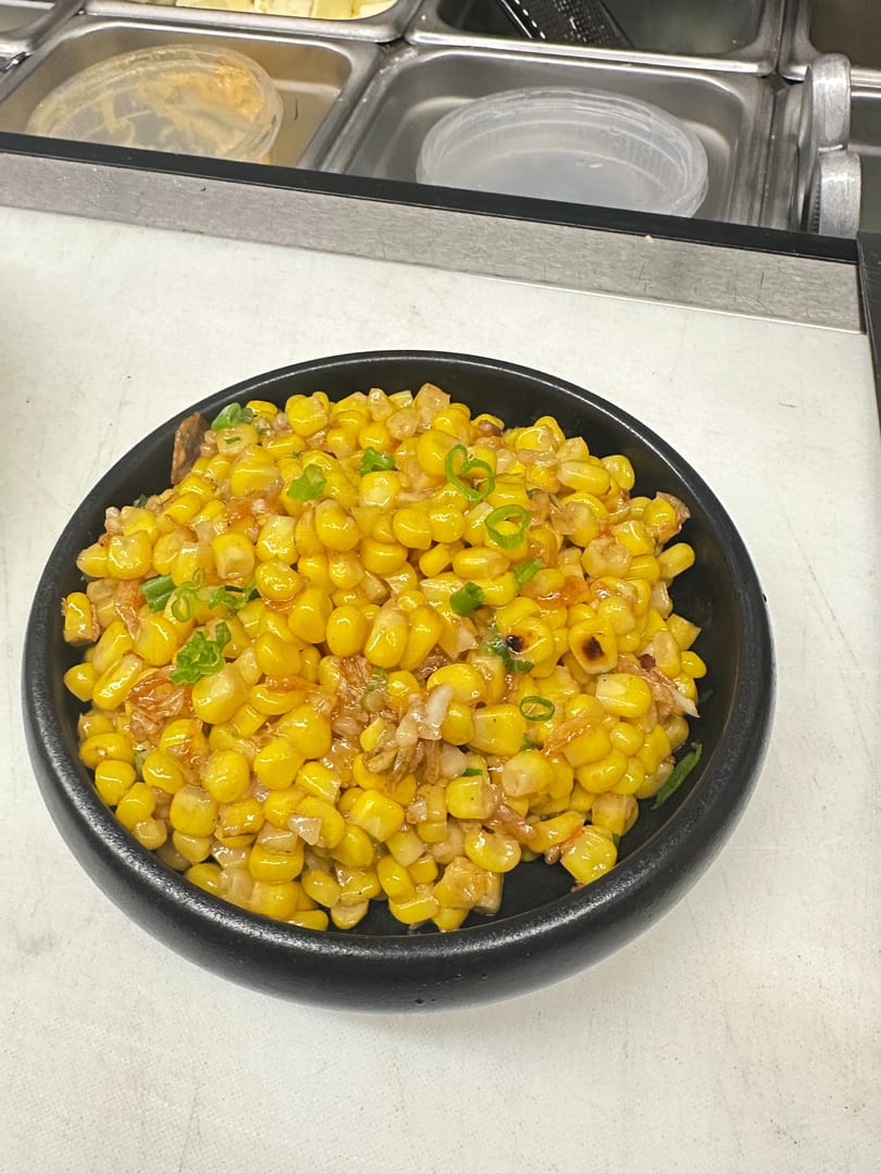 A black bowl filled with yellow corn kernels, green onions, and a light sauce.