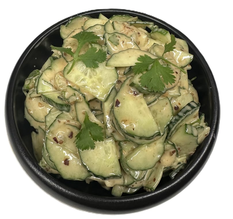 Cucumber salad with creamy dressing and cilantro in a black bowl.