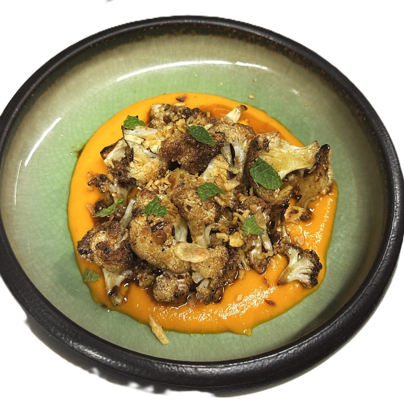 Roasted cauliflower florets with mint and crispy garlic, served on a vibrant orange puree in a green bowl.