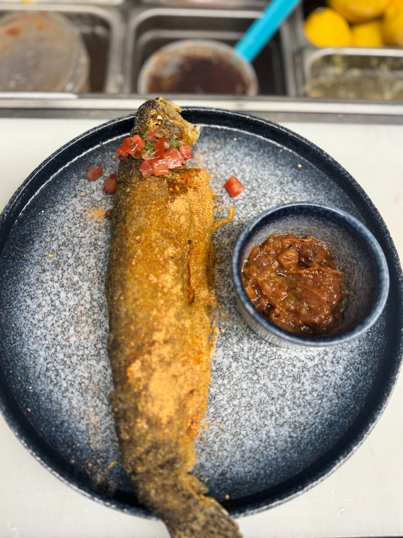 Crispy fried whole fish topped with diced tomatoes, served with a side of brown sauce.